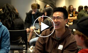 Lei Jin sits in the Victor K Wilson Memorial Hall Ballroom surrounded by other students laughing during International Coffee Hour